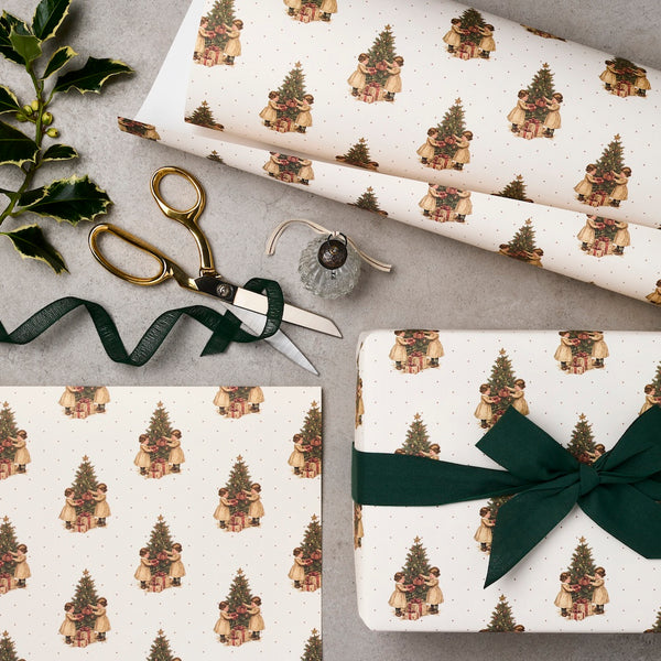 Gift wrap with Christmas tree design, scissors, and ribbon on a gray surface.