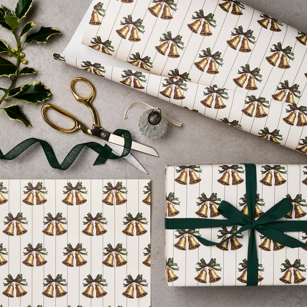Gift wrap with bell pattern, scissors, and ribbon on a gray surface