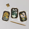 Three floral embroidered cards on white paper with a gold pen and inkwell.