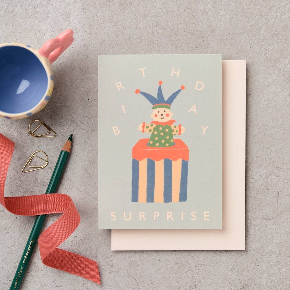Birthday card with clown illustration on a textured surface with stationery items.