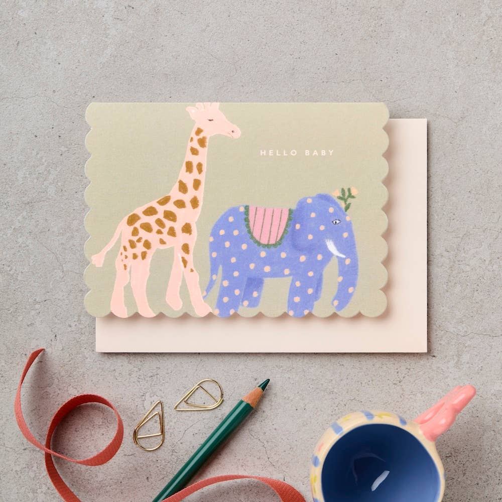 Greeting card with a giraffe and elephant design on a textured surface with stationery items.