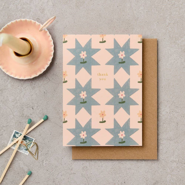 Greeting card with geometric pattern and 'thank you' text on a textured surface with matches and a small dish.