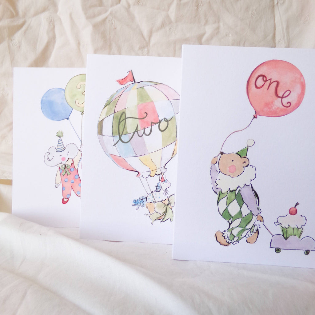 Three children's greeting cards with illustrations of a clown, hot air balloon, and balloons on a textured surface.