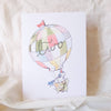 Card with a colorful hot air balloon and teddy bear design on a soft beige background