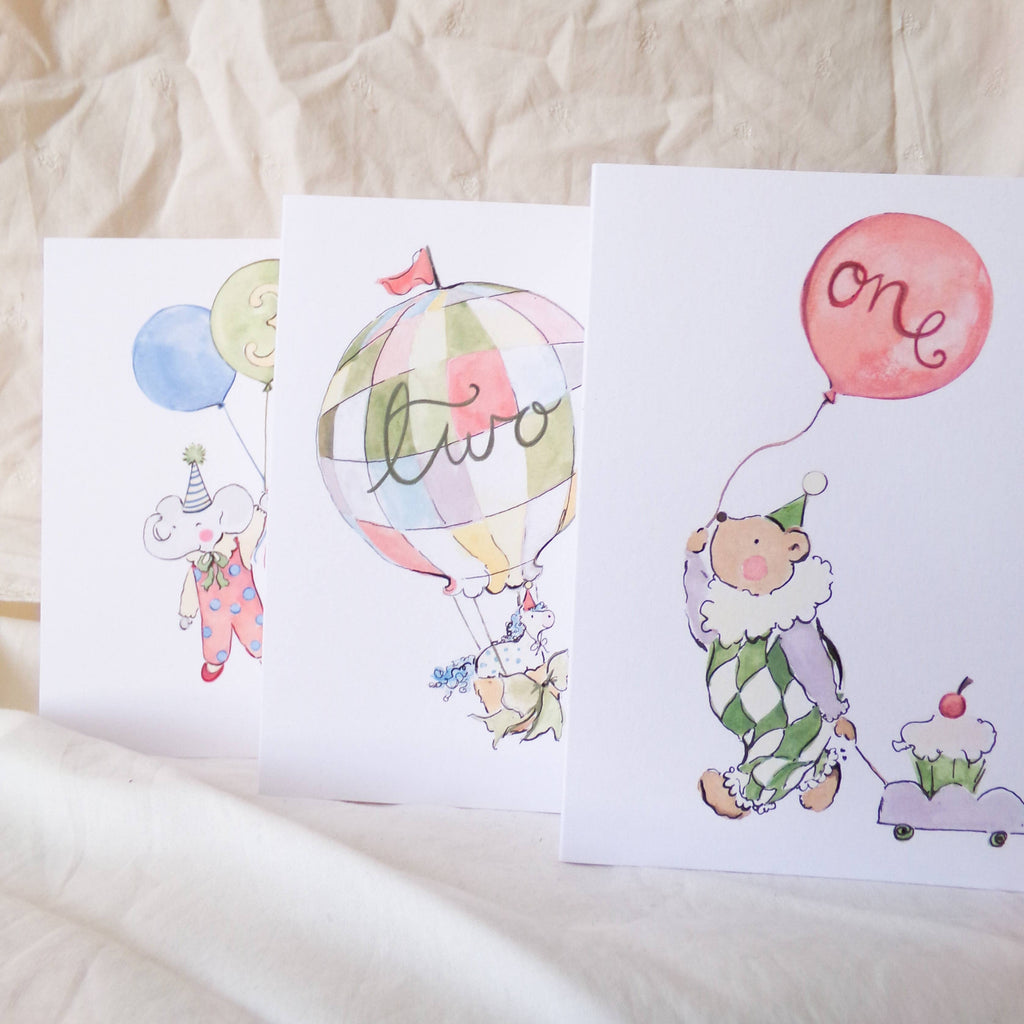 Three children's greeting cards with illustrations of a clown, hot air balloon, and balloons on a textured surface.