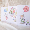 Three children's greeting cards with illustrations of a clown, hot air balloon, and balloons on a textured surface.