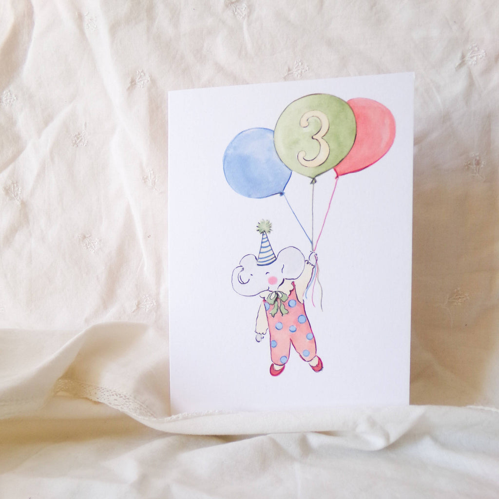 Card with a bear holding balloons and the number 3 on a beige fabric background