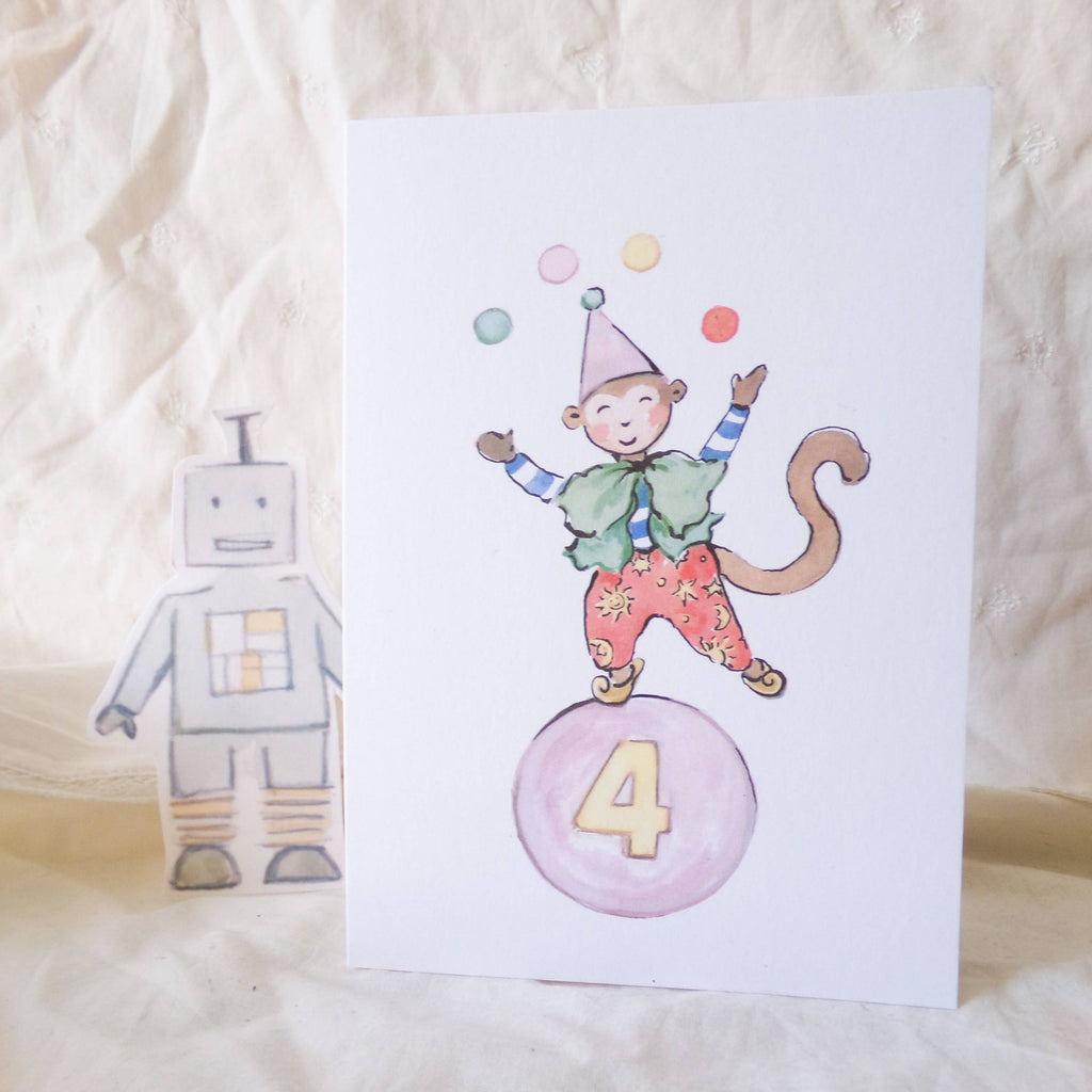 Children's birthday card with monkey juggling on a ball, robot, and number 4 on a soft fabric background.