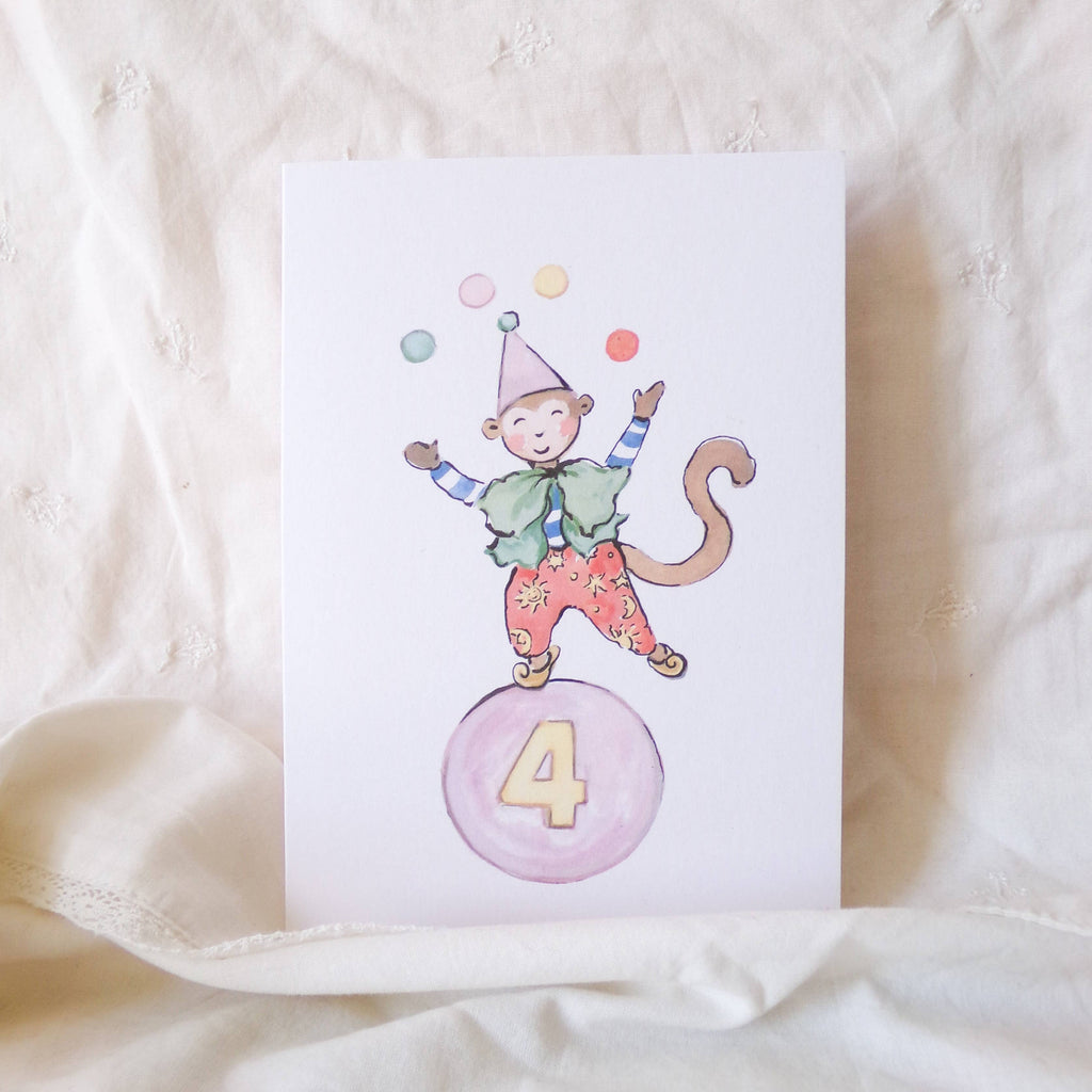 Card with a monkey character on a pink ball with the number 4, on a beige fabric background.