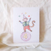 Card with a monkey character on a pink ball with the number 4, on a beige fabric background.
