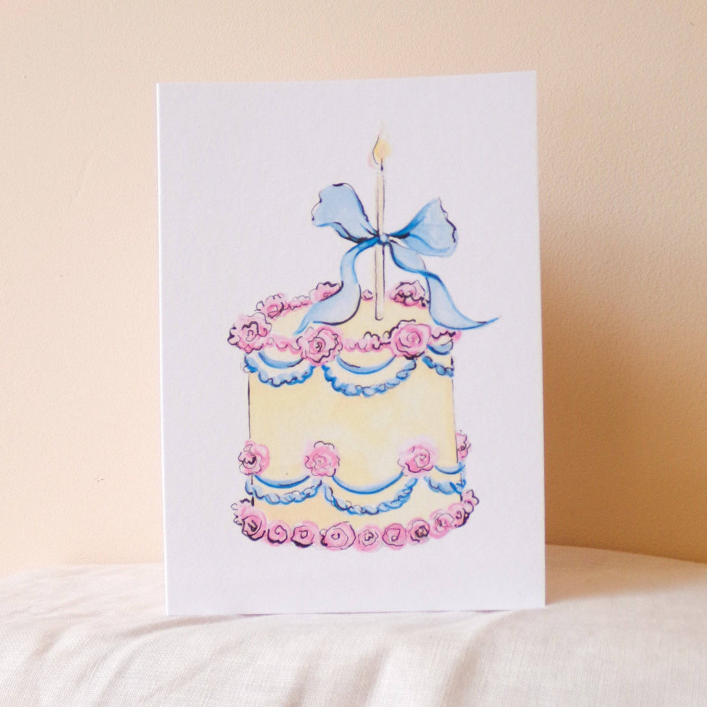 Greeting card with a cake illustration featuring pink flowers and a blue bow on a beige background