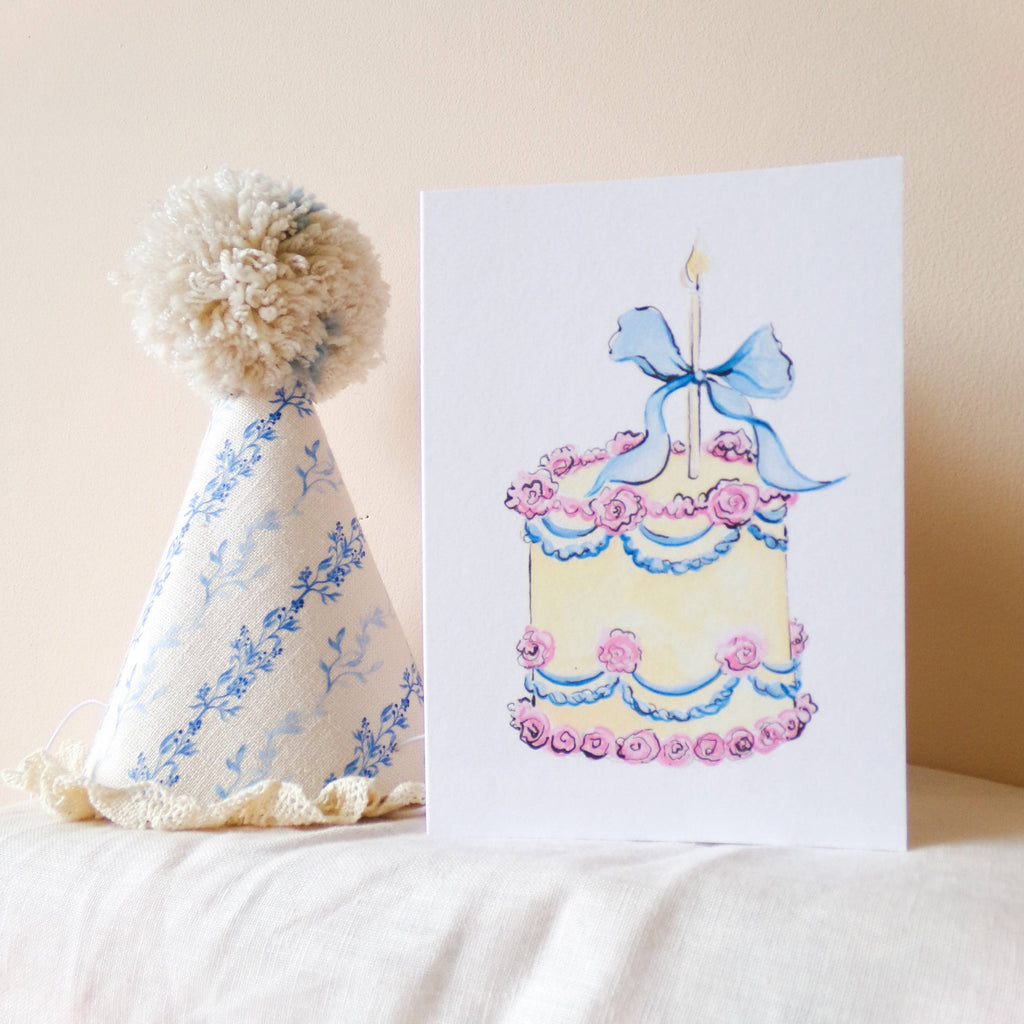 Children's birthday hat and card with cake illustration on a white surface