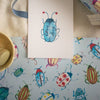 Note card with a beetle design on a table with colorful beetle-patterned paper and a bowl.
