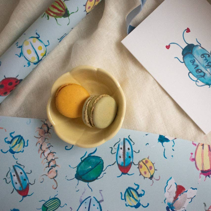 Colorful insect illustrations on paper and fabric with a small bowl of macarons.