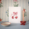 Decorative items including a card with cherries and a bow, a bowl, and a candle holder with a bow on a striped floral background.