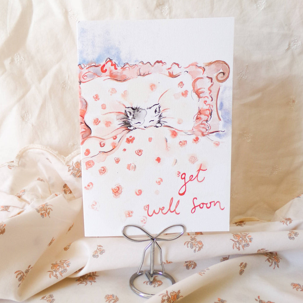 Greeting card with a cat illustration and 'get well soon' text on floral fabric.