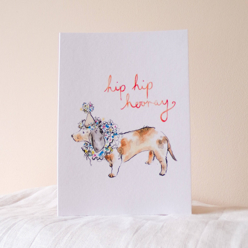 Card with a dog illustration and 'hip hip hooray' text on a white surface.