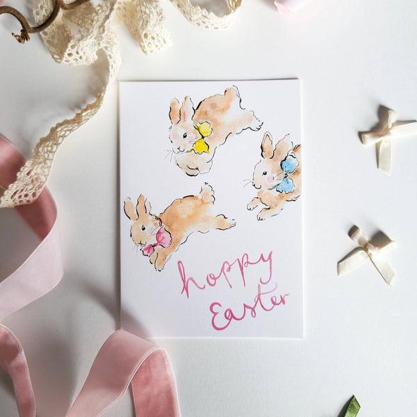 Easter card with bunnies and 'Happy Easter' text, surrounded by ribbons and decorative elements on a white background.