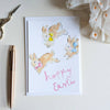 Easter card with bunnies and 'Happy Easter' text on a white surface with a pen and decorative bow.