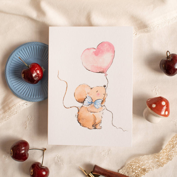 Card with a mouse holding a heart-shaped balloon on a textured surface with cherries and a pen.