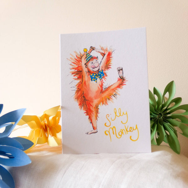 Greeting card with a colorful monkey illustration on a white surface with decorative elements.