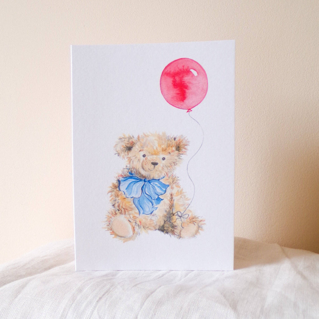 Card with a teddy bear holding a red balloon on a white background