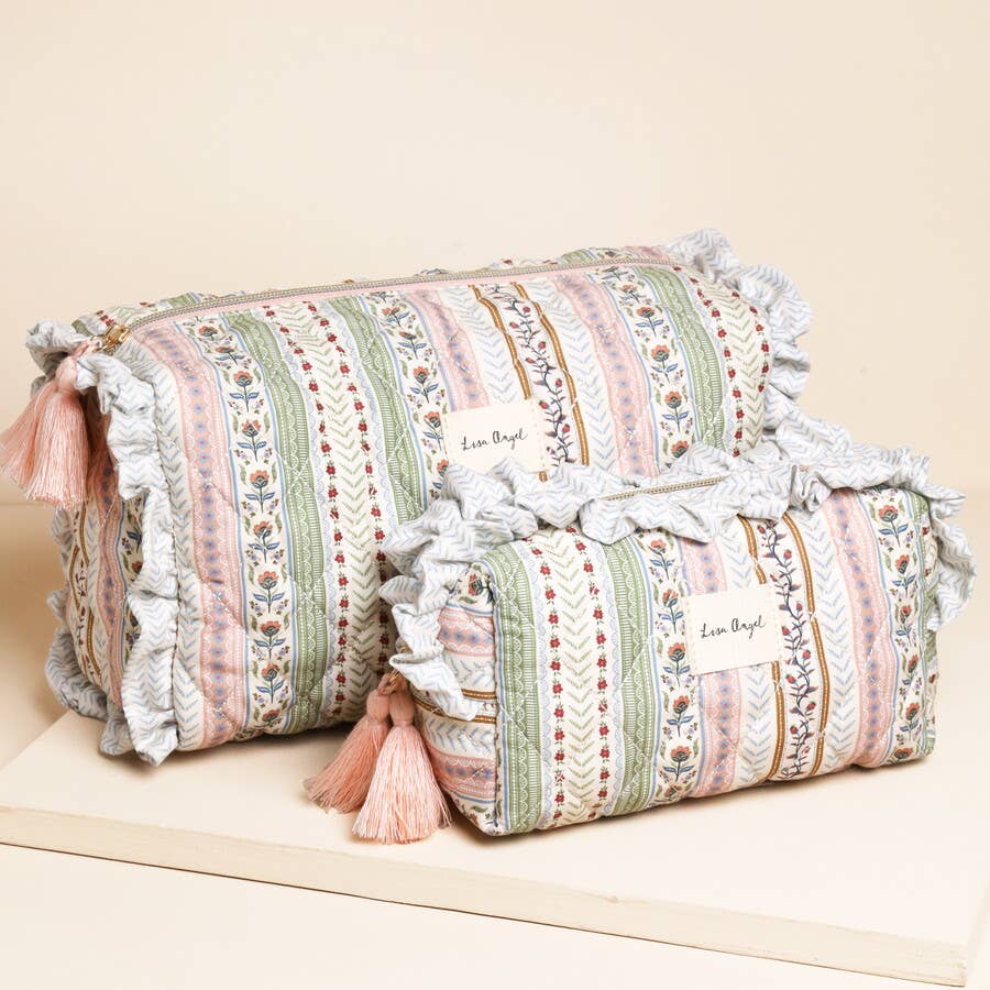 Decorative cylindrical pillows with floral patterns and tassels on a beige surface