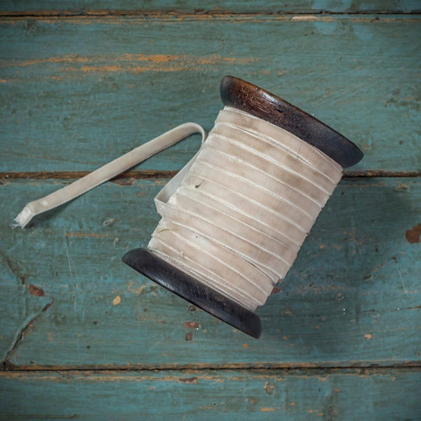 A spool of cream-colored ribbon with dark brown plastic ends, lying on a distressed teal wooden surface.