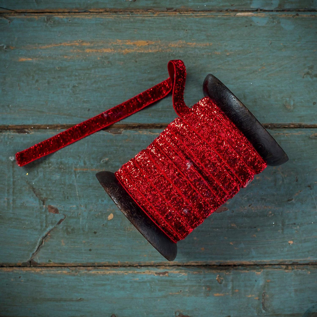 A spool of red glitter ribbon with a matching loose tail, resting on a distressed teal wooden surface.