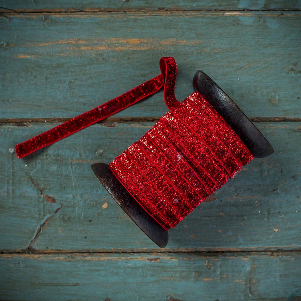 A spool of red glitter ribbon with a matching loose tail, resting on a distressed teal wooden surface.