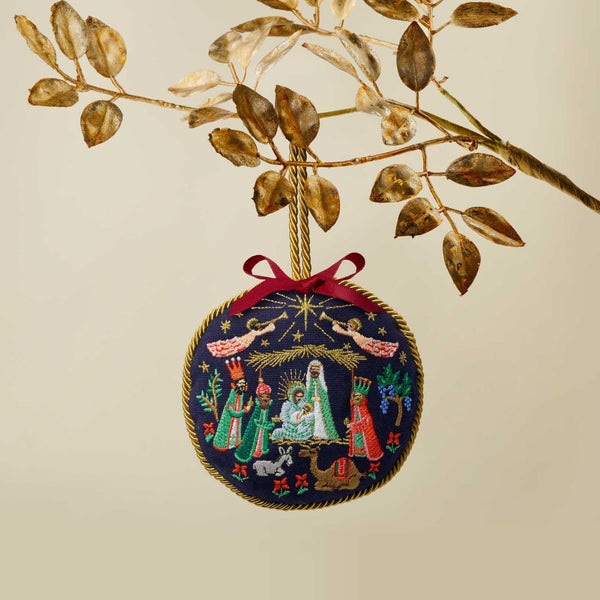 Decorative Christmas ornament with nativity scene design hanging from a branch.