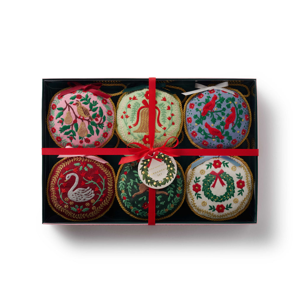 Set of six decorative Christmas ornaments in a black box with a red ribbon on a white background