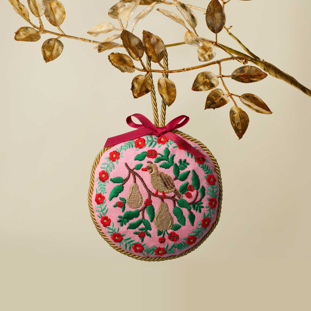 Decorative Christmas ornament with birds and flowers on a branch against a beige background