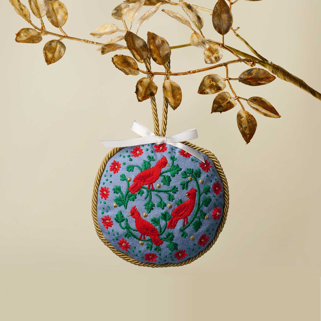 Decorative ornament with embroidered design of red birds and flowers, hanging from a branch.
