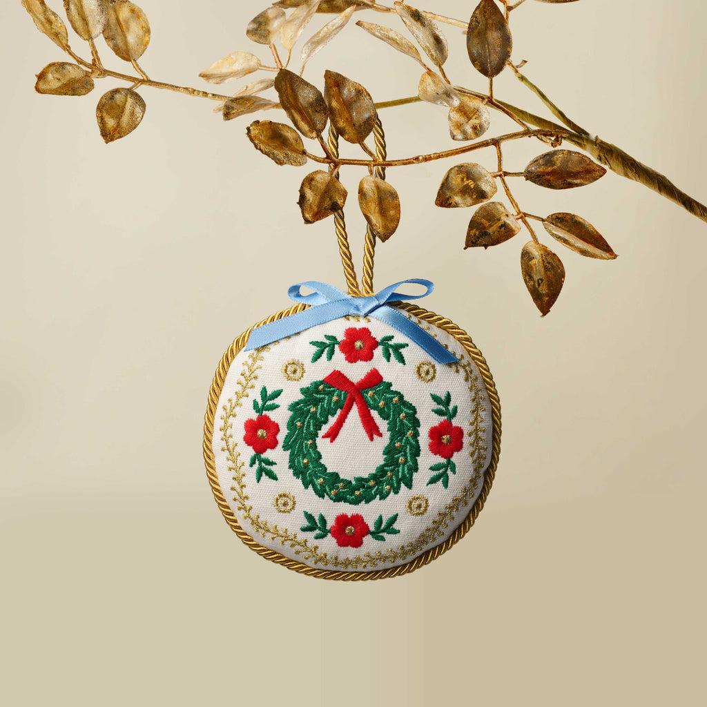 Decorative Christmas ornament with a wreath design hanging from a branch.