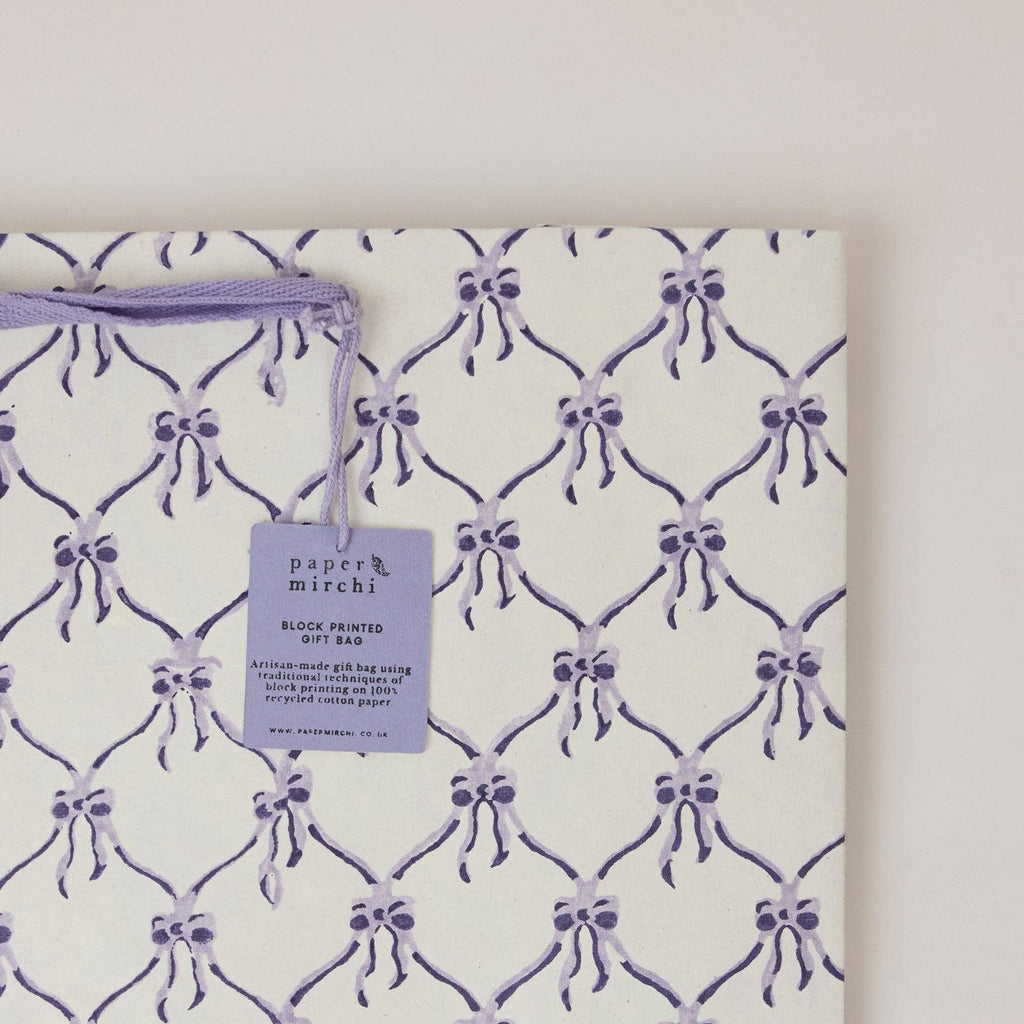 Block printed gift bag with purple bow pattern and 'paper mirchi' tag on a white background
