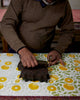 Person working with a dark object on a table with a floral tablecloth
