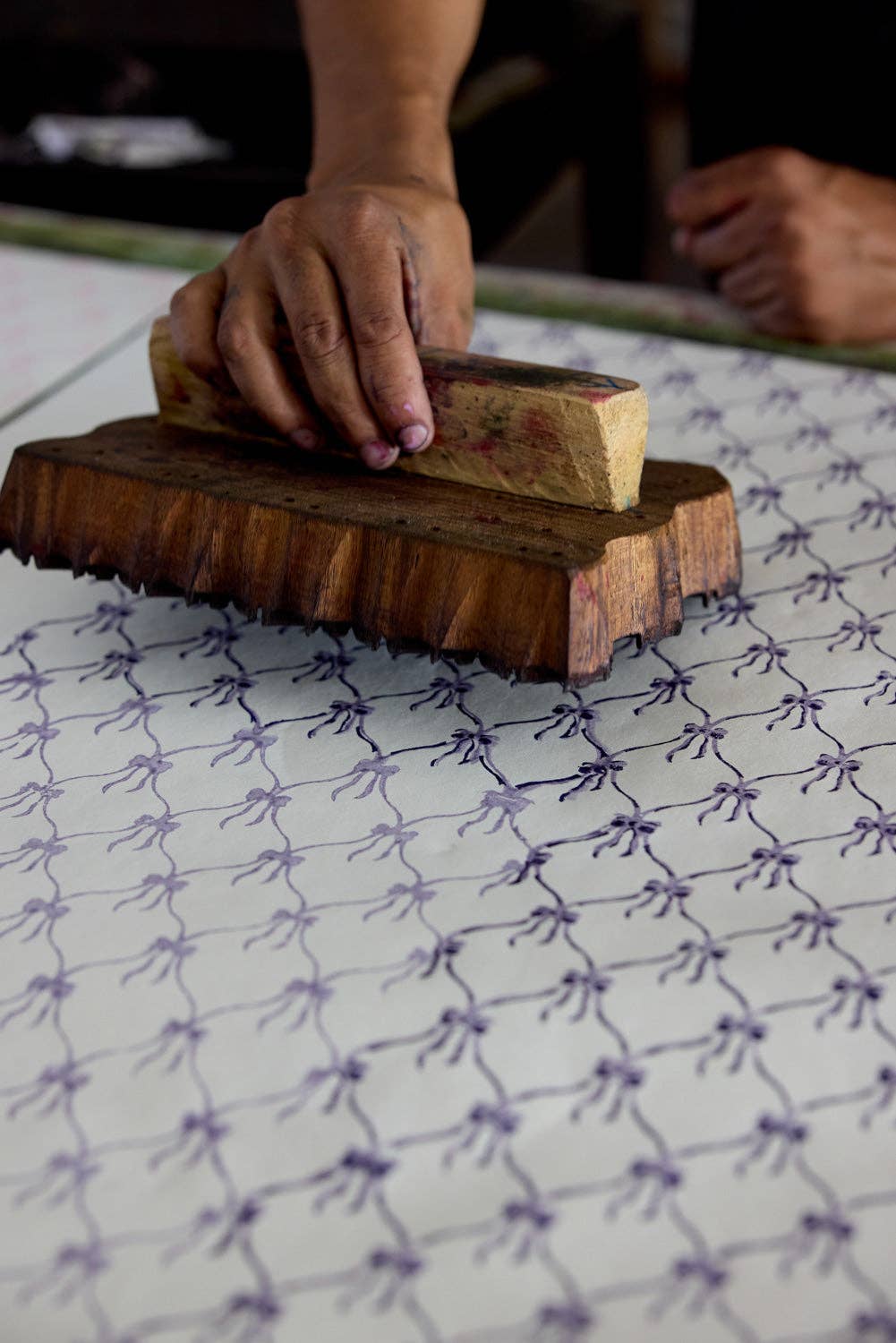 Person using a wooden block to press a block of soap onto a textured surface.