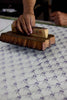 Person using a wooden block to press a block of soap onto a textured surface.