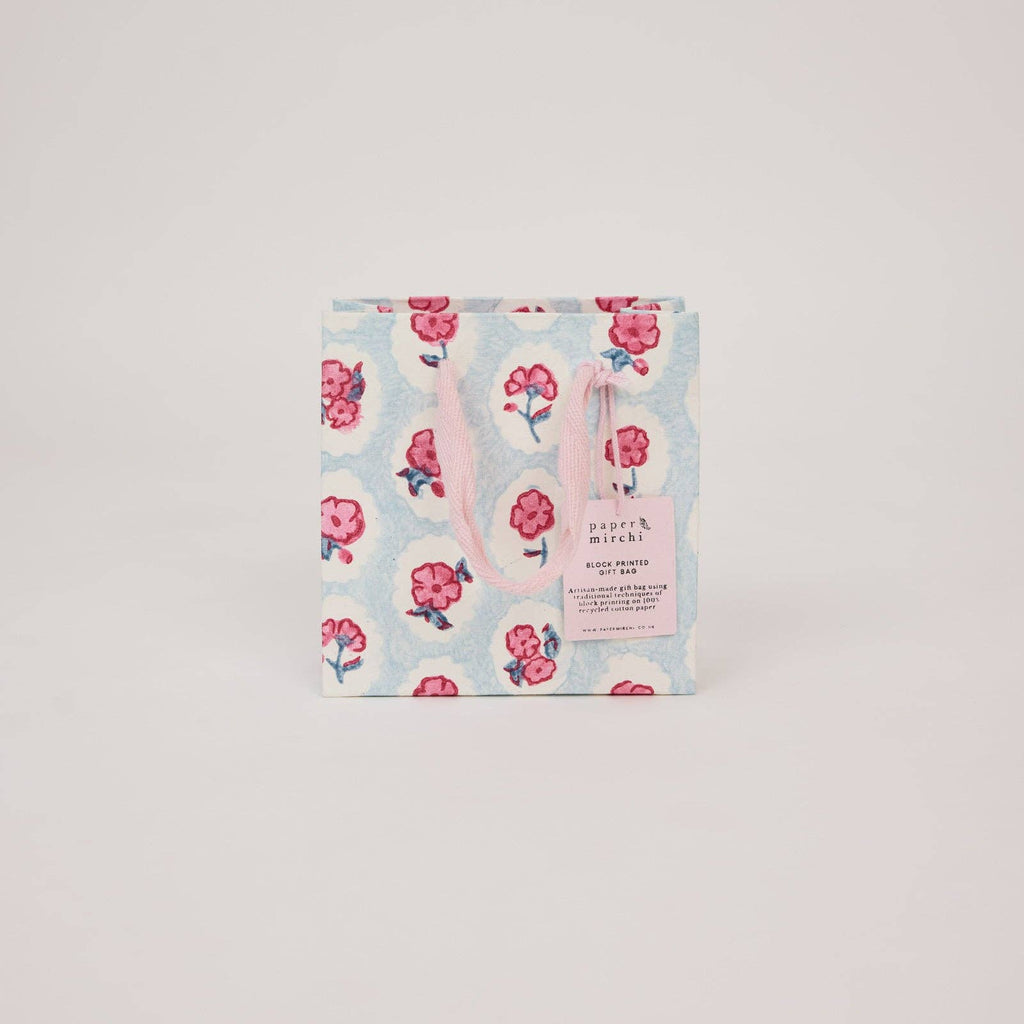 Floral patterned gift bag with pink handle on a light gray background