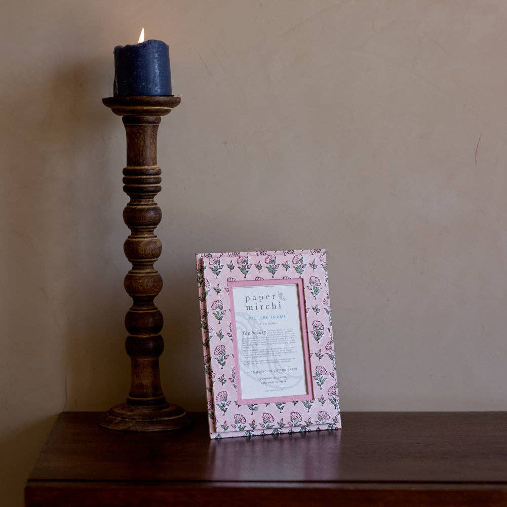 Wooden candlestick with a lit blue candle and a framed card on a wooden surface against a beige wall.
