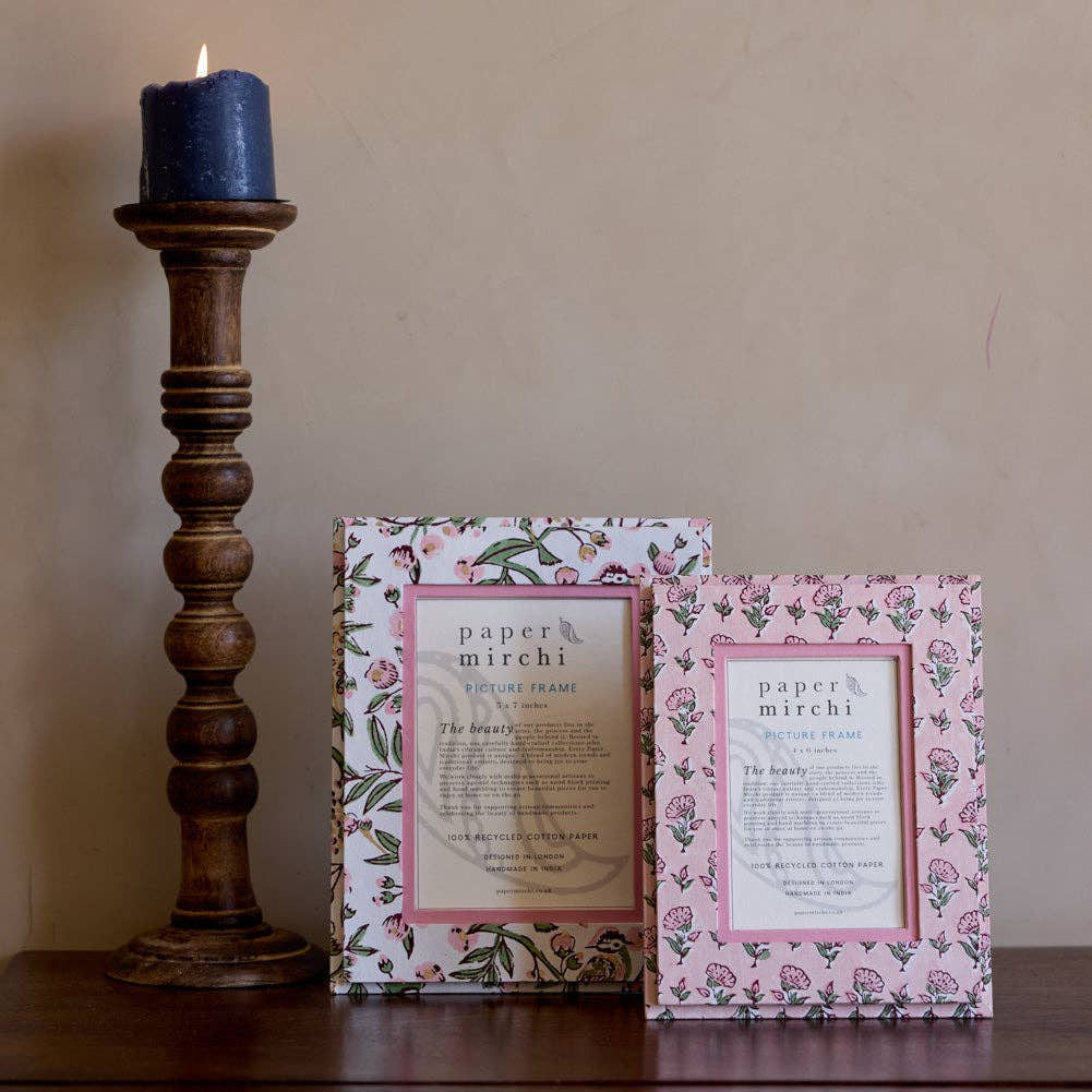 Two framed prints on a wooden surface with a candle in the background.