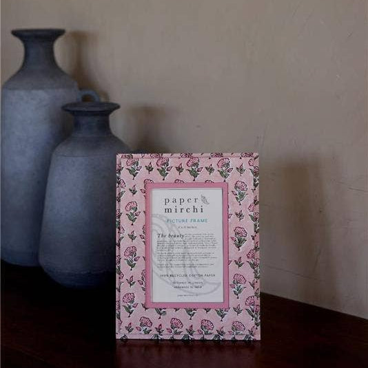 Pink floral framed picture on a wooden surface with gray vases in the background
