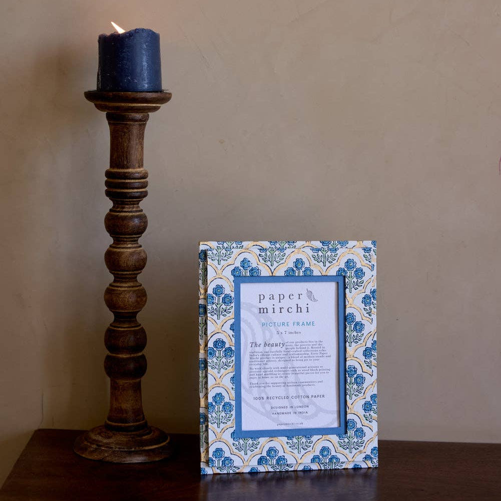 Decorative candle holder with a blue candle and a framed print on a wooden surface.