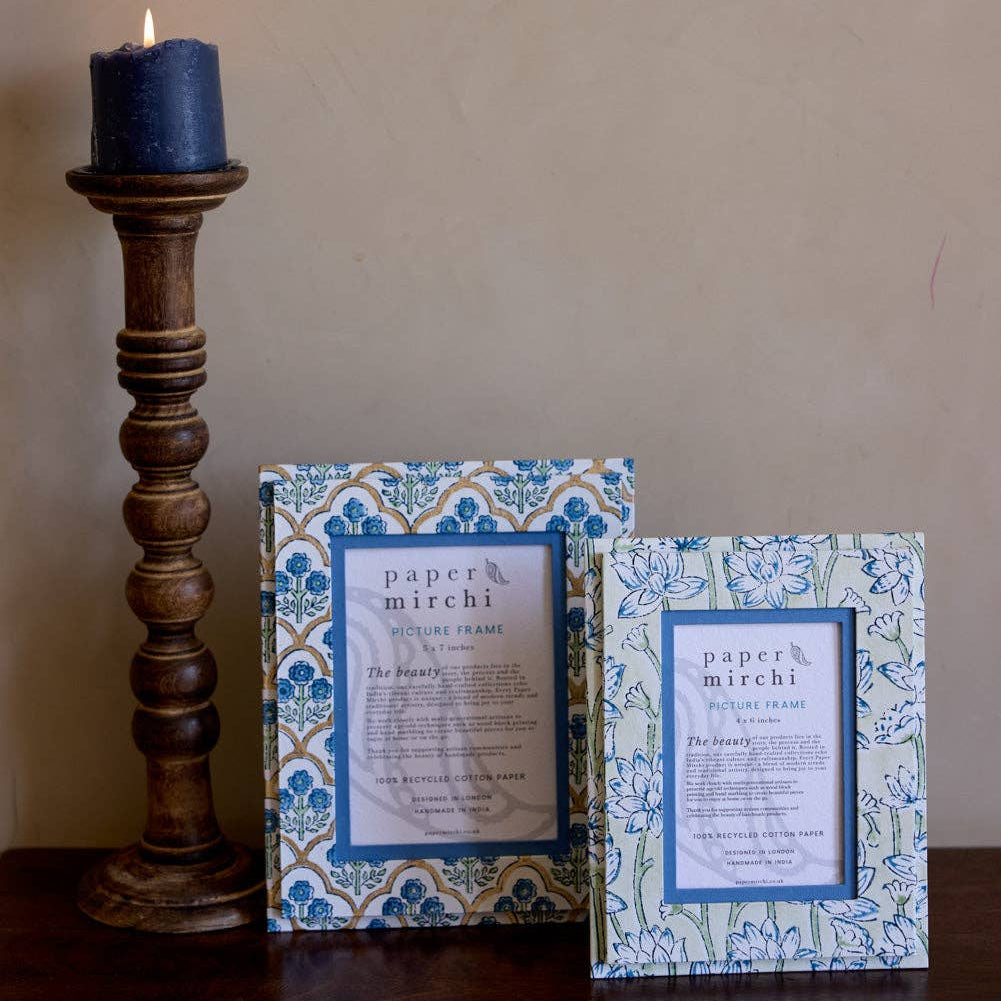 Two decorative boxes with floral patterns next to a lit candle on a wooden surface.