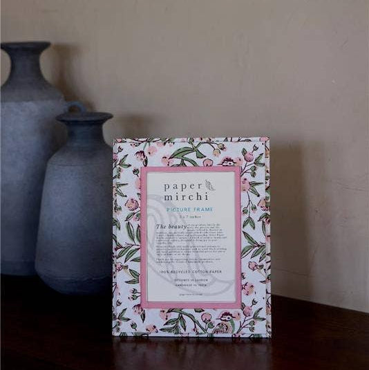 Decorative box with floral design and text on a wooden surface with vases in the background