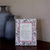 Decorative box with floral design and text on a wooden surface with vases in the background
