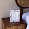 Framed floral print on a wooden nightstand next to a bed with a wicker headboard.