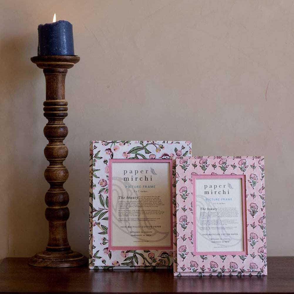 Two framed prints on a wooden surface with a candle in the background.
