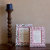Two framed prints on a wooden surface with a candle in the background.